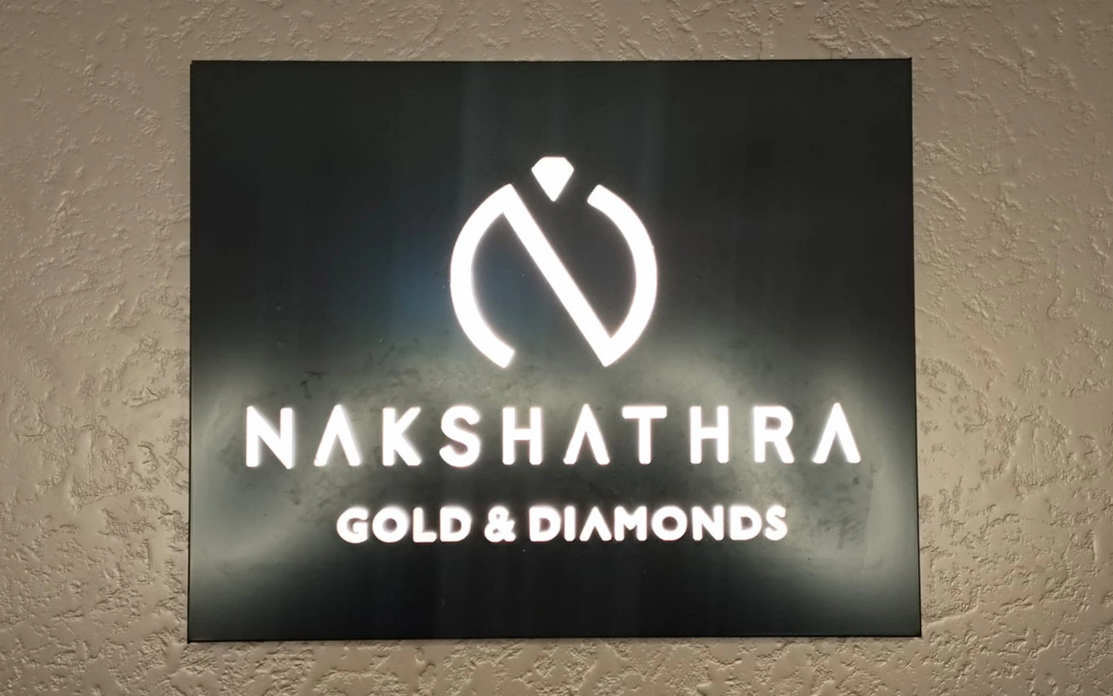 Illuminated Nakshathra Gold and Diamonds logo panel on a textured wall